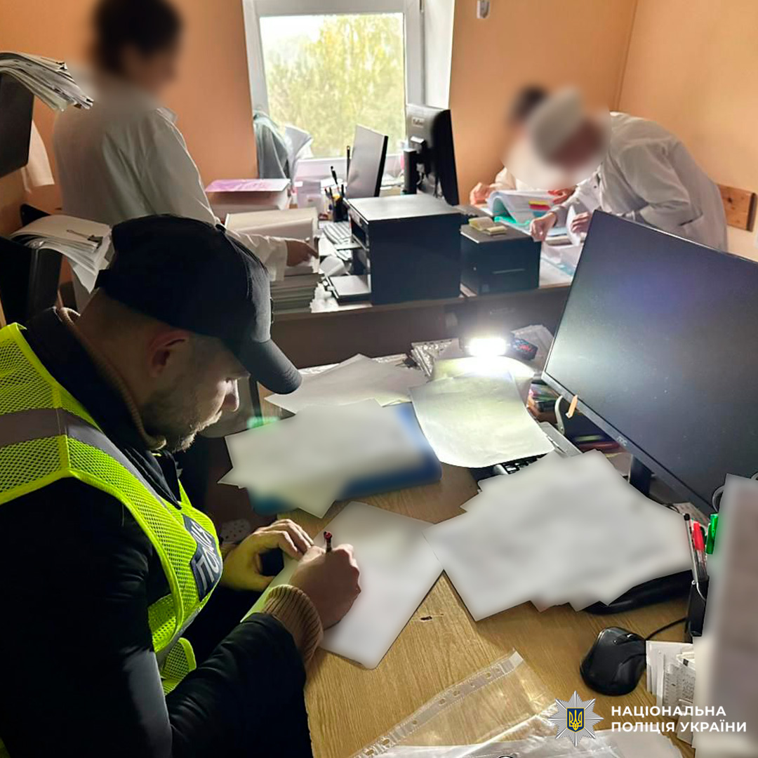 Поліцейський у світловідбивальному жилеті перевіряє документи в офісі. Поруч  двоє медиків у білих халатах.