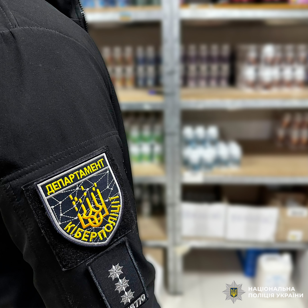 Співробітник кіберполіції України у чорній куртці з шевроном. На фоні склад із товарами.