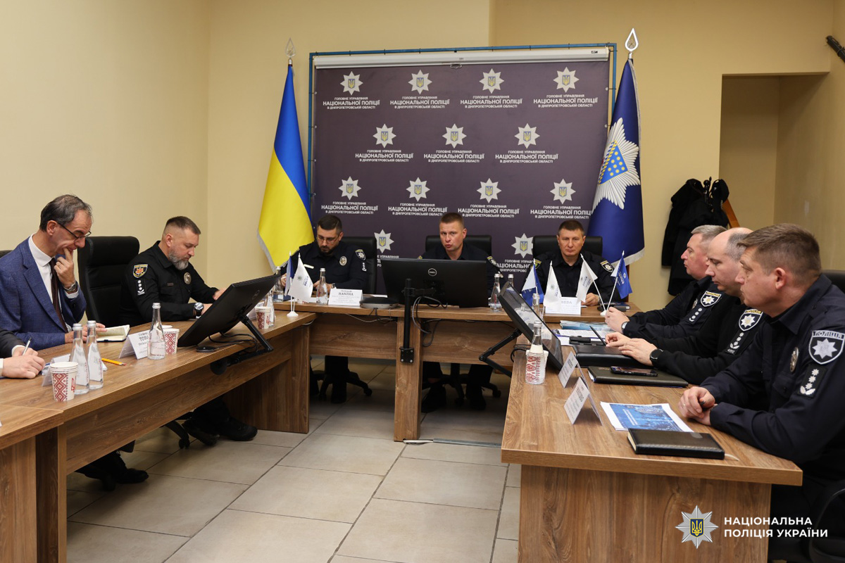 Офіційна зустріч співробітників Національної поліції України та ЄС. Учасники в поліцейській формі сидять за столами, розташованими у формі літери U, обговорюють документи, користуються ноутбуками та мікрофонами. На задньому плані — банер з емблемою поліції, державний прапор України та прапор поліції