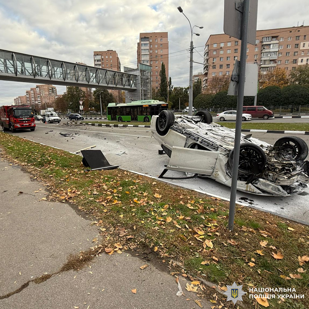 Автомобіль перевернутий на дах посеред міської дороги після аварії. На вулиці видно розкидані уламки.