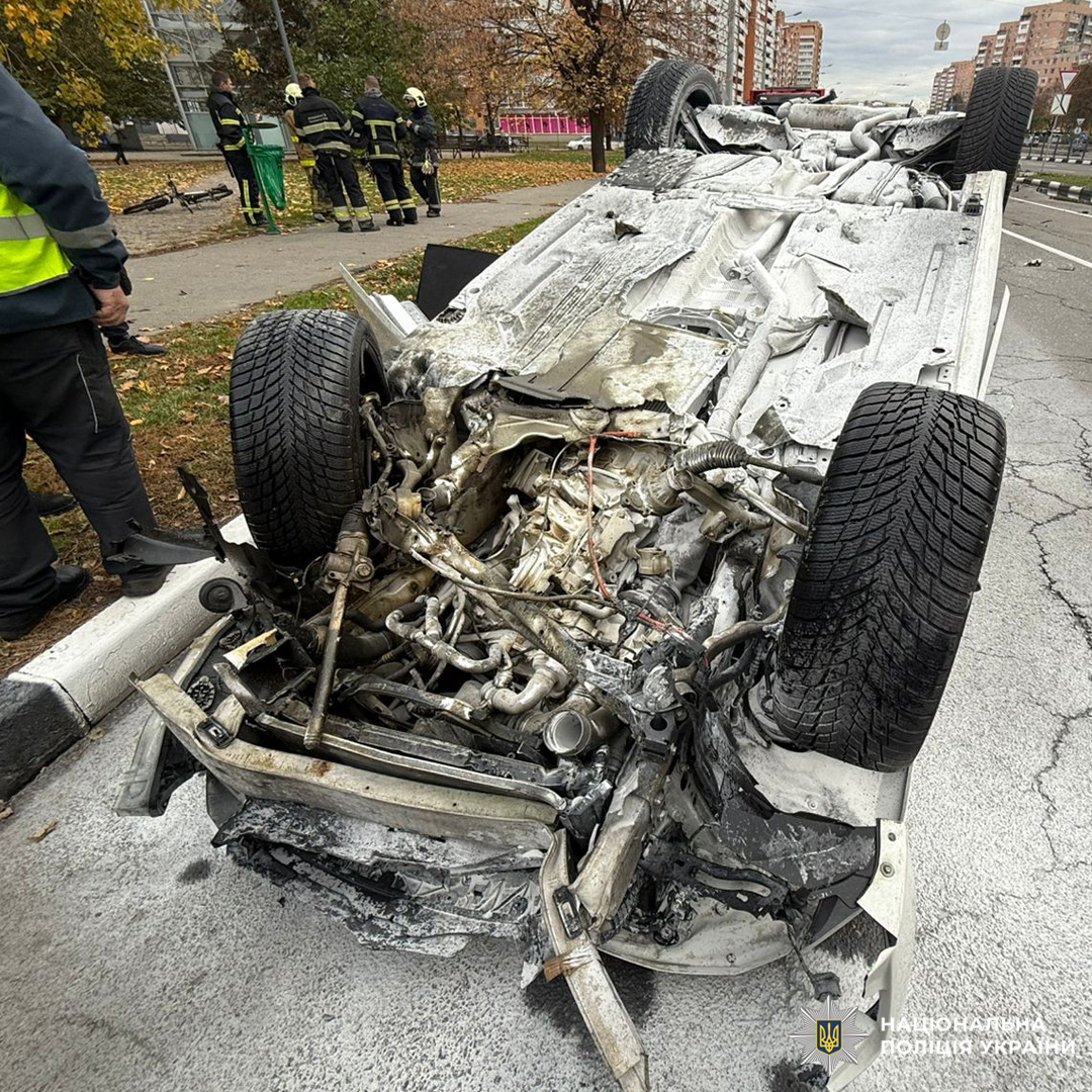 Білий автомобіль перевернутий на дах посеред міської дороги після аварії. Навколо розкидані уламки.