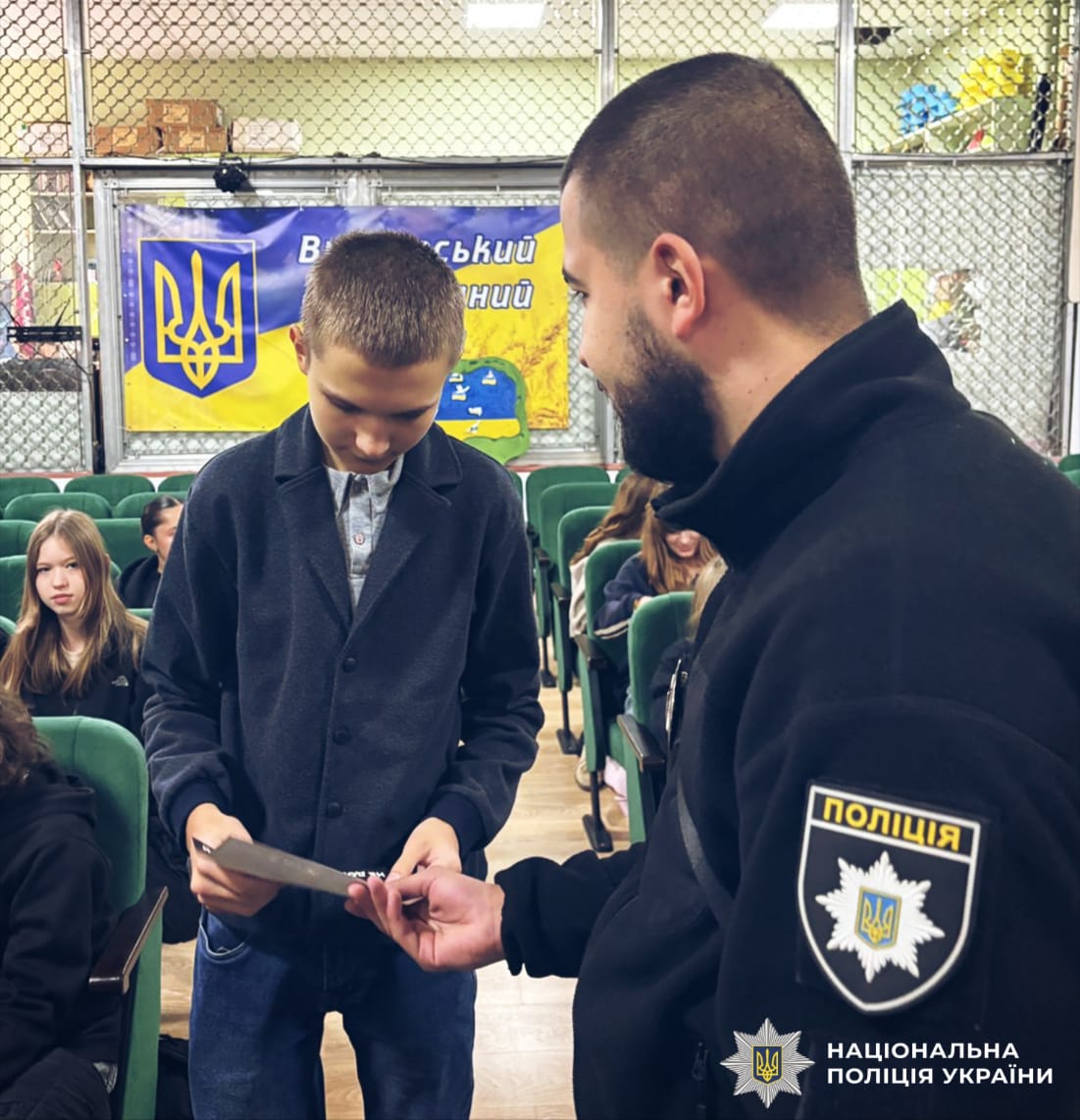 На фото поліцейський надає учню листівку.