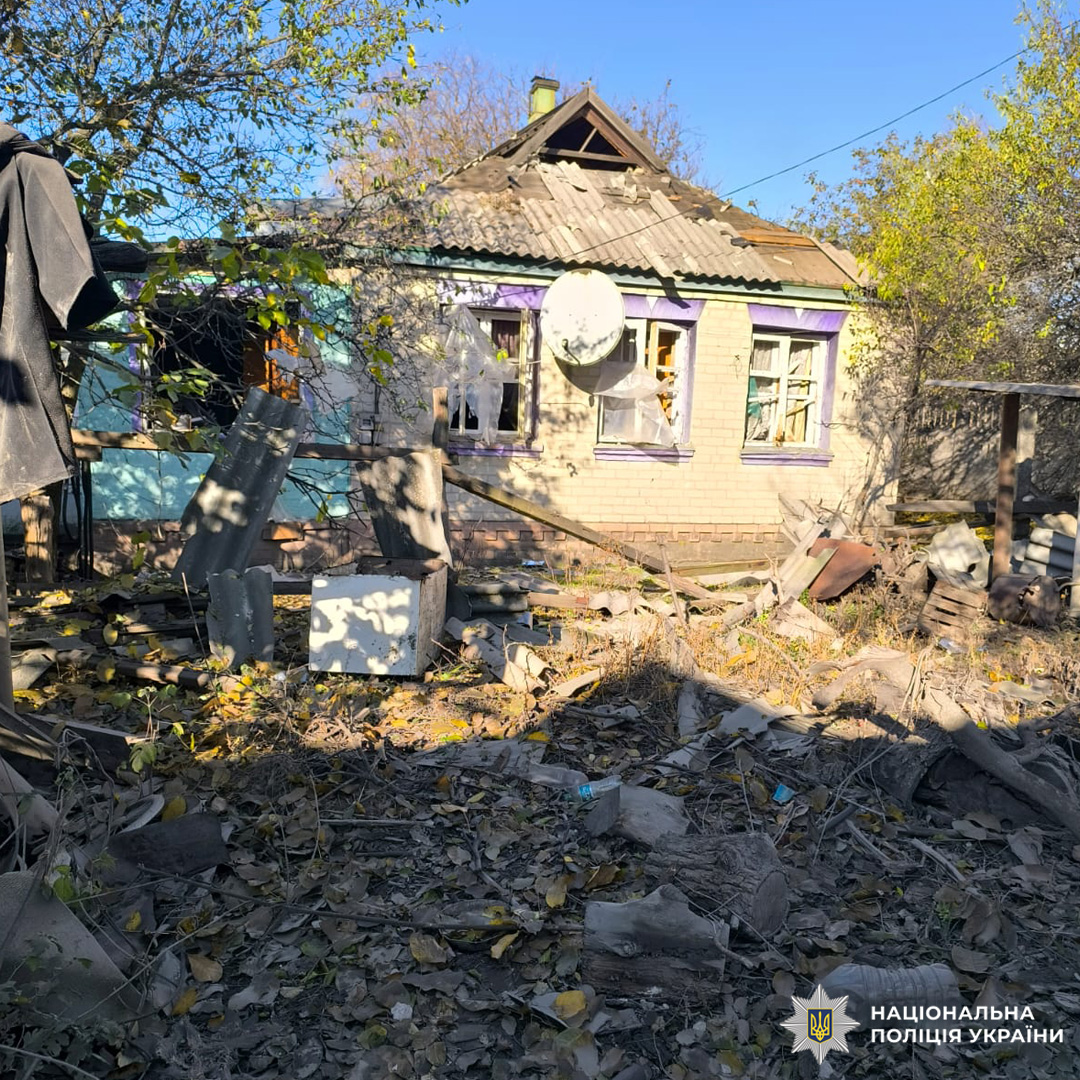 Одноповерховий будинок із двосхилим дахом і супутниковою антеною на фасаді. Вікна розбиті, навколо уламки меблів, листя та покинуті речі. Двір заріс, будівля має ознаки занедбаності або пошкодження.