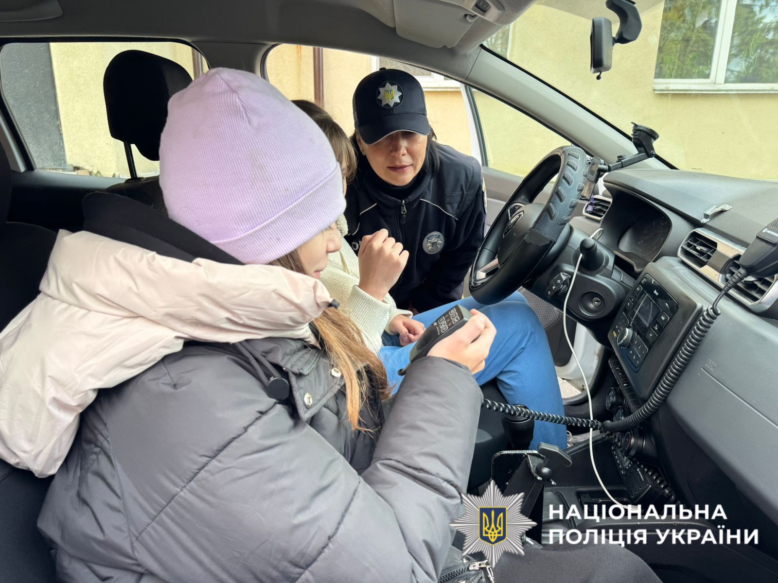 На фото зображені діти, які оглядають службовий поліцейський автомобіль.