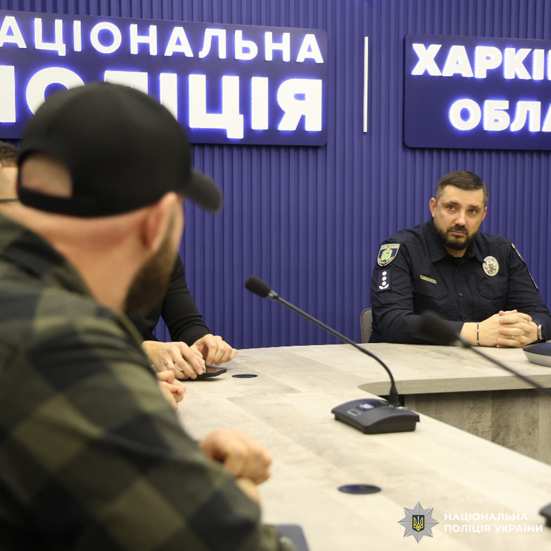 У конференц-залі триває обговорення: кілька осіб сидять за столом, один із поліцейських уважно слухає. На фоні підсвічені написи «Національна поліція».