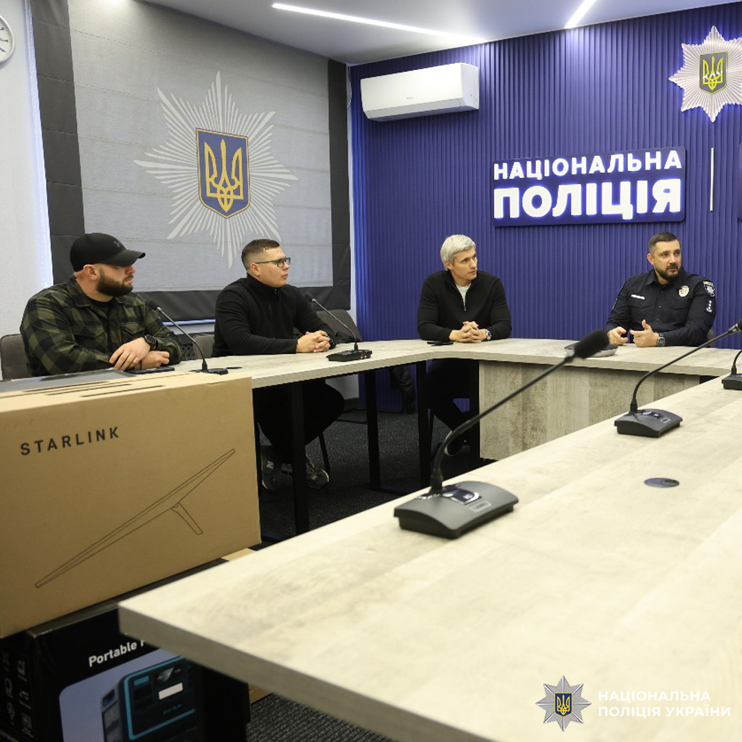 У конференц-залі триває обговорення: кілька осіб сидять за столом, один із поліцейських уважно слухає. На фоні підсвічені написи «Національна поліція».