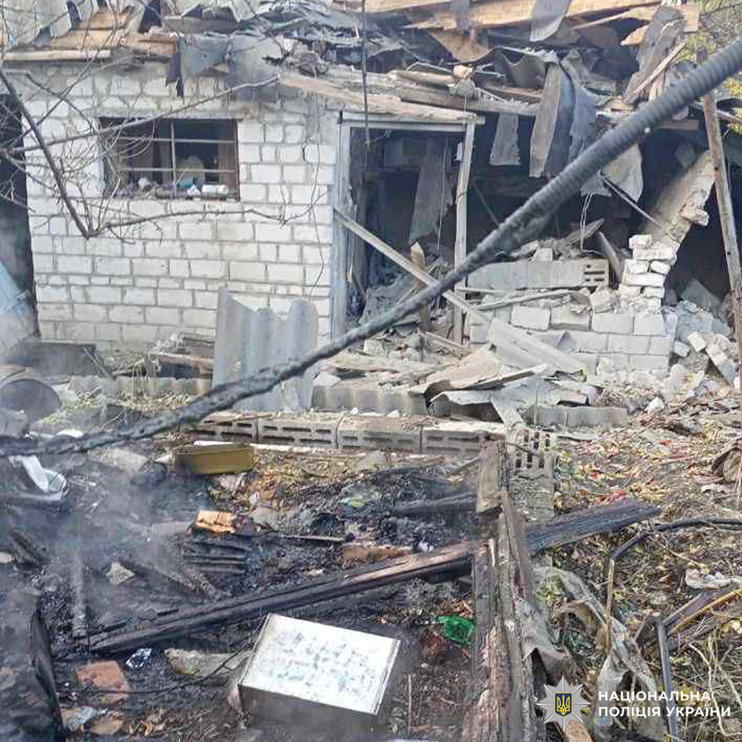 Зруйнована будівля з бетонних блоків і дерева: обвалені стіни, пошкоджений дах, сліди пожежі, уламки. Серед руїн обгорілий предмет із сіткою або таблицею.