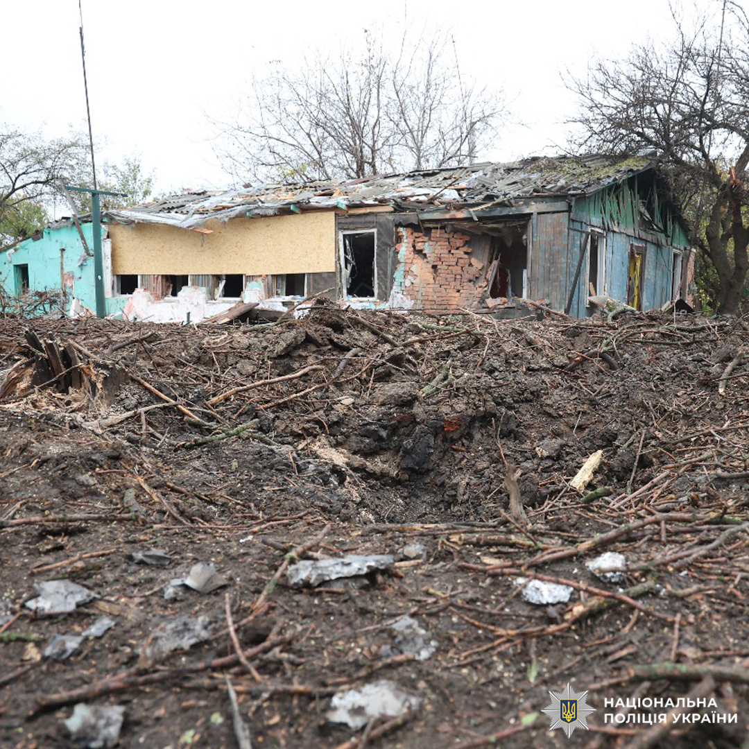 Зруйнована будівля з великим кратером перед фасадом, обвалені конструкції, уламки, пошкоджені вікна.