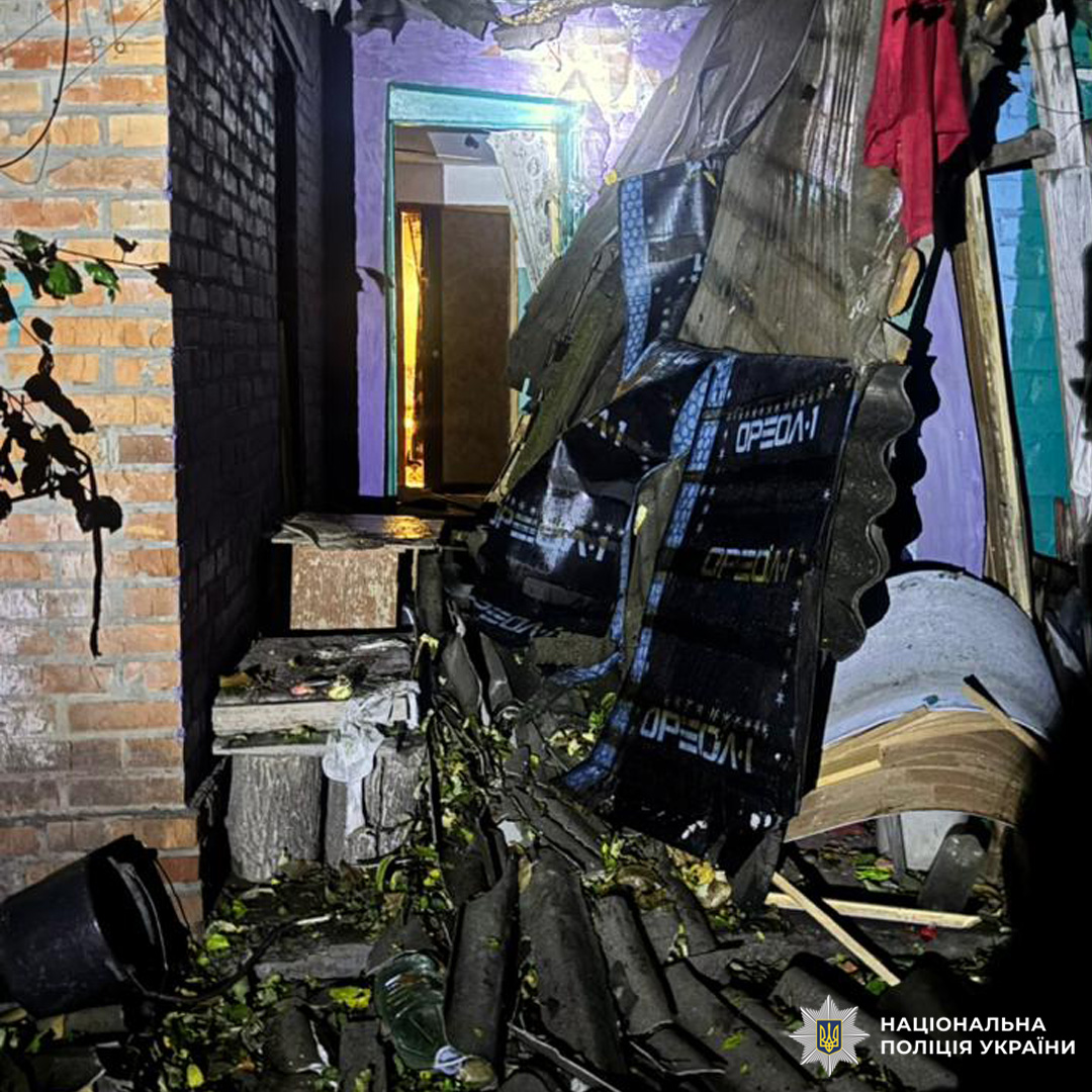 Пошкоджене внутрішнє приміщення з яскравими стінами (фіолетовий, бірюзовий), уламками даху, ізоляційними матеріалами та частково обваленою конструкцією. Видно цегляну стіну та прохід до іншої кімнати.