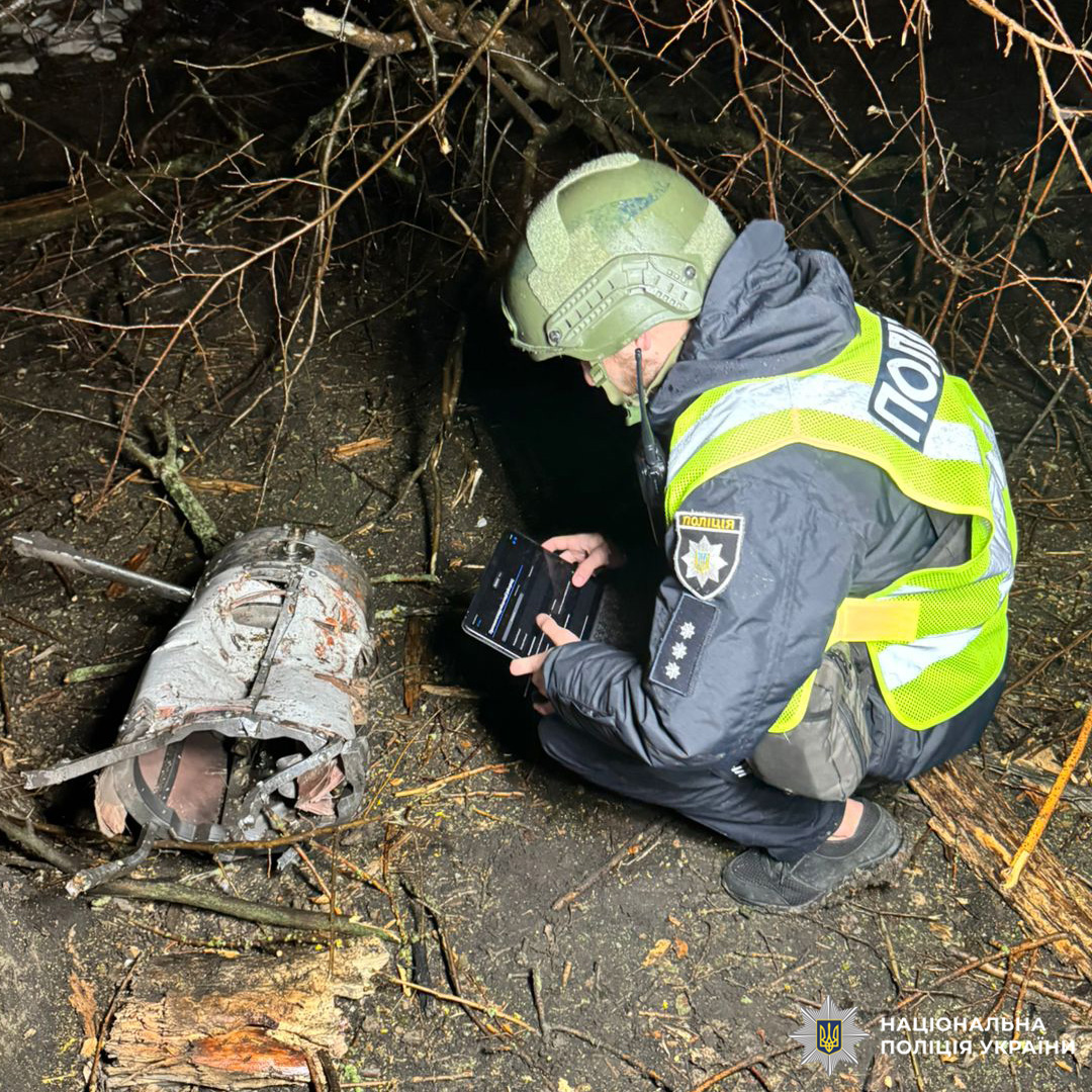 Поліцейський у захисному спорядженні фіксує пошкоджений металевий об’єкт у лісовій зоні вночі.