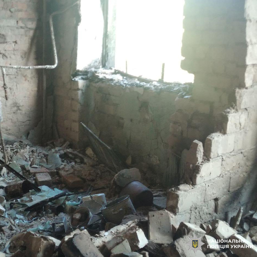 Зруйноване приміщення з пошкодженими цегляними стінами, розбитим вікном і розкиданими уламками. Видно металеві конструкції, труби та залишки будівельних матеріалів.