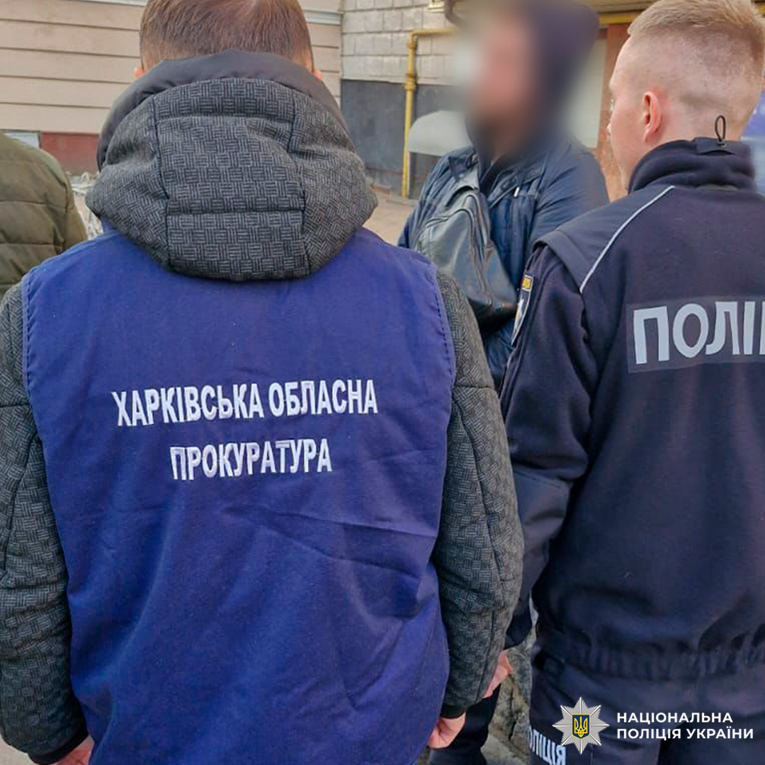 На зображенні зафіксовано групу осіб біля будівлі, серед яких працівники правоохоронних органів. Один із них одягнений у синій жилет з написом «Харківська обласна прокуратура», інший у куртку з написом «Поліція». Обличчя третьої особи розмито для захисту особистих даних.