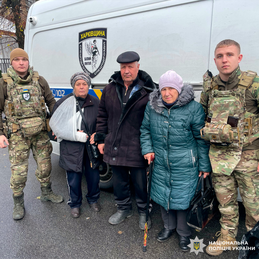 Двоє поліцейських, троє літні цивільні особи в зимовому одязі. Один із цивільних тримає палицю, що свідчить про обмежену мобільність. Сцена ймовірно пов’язана з евакуацією.