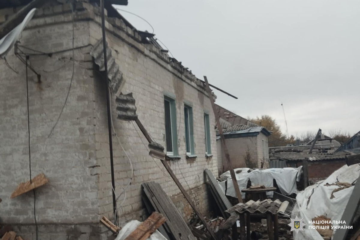 На фото цегляна споруда з частково обваленим дахом, розкиданими будівельними матеріалами та деформованими металевими листами. Вікна залишились цілими, однак загальний стан об’єкта свідчить про значні руйнування.