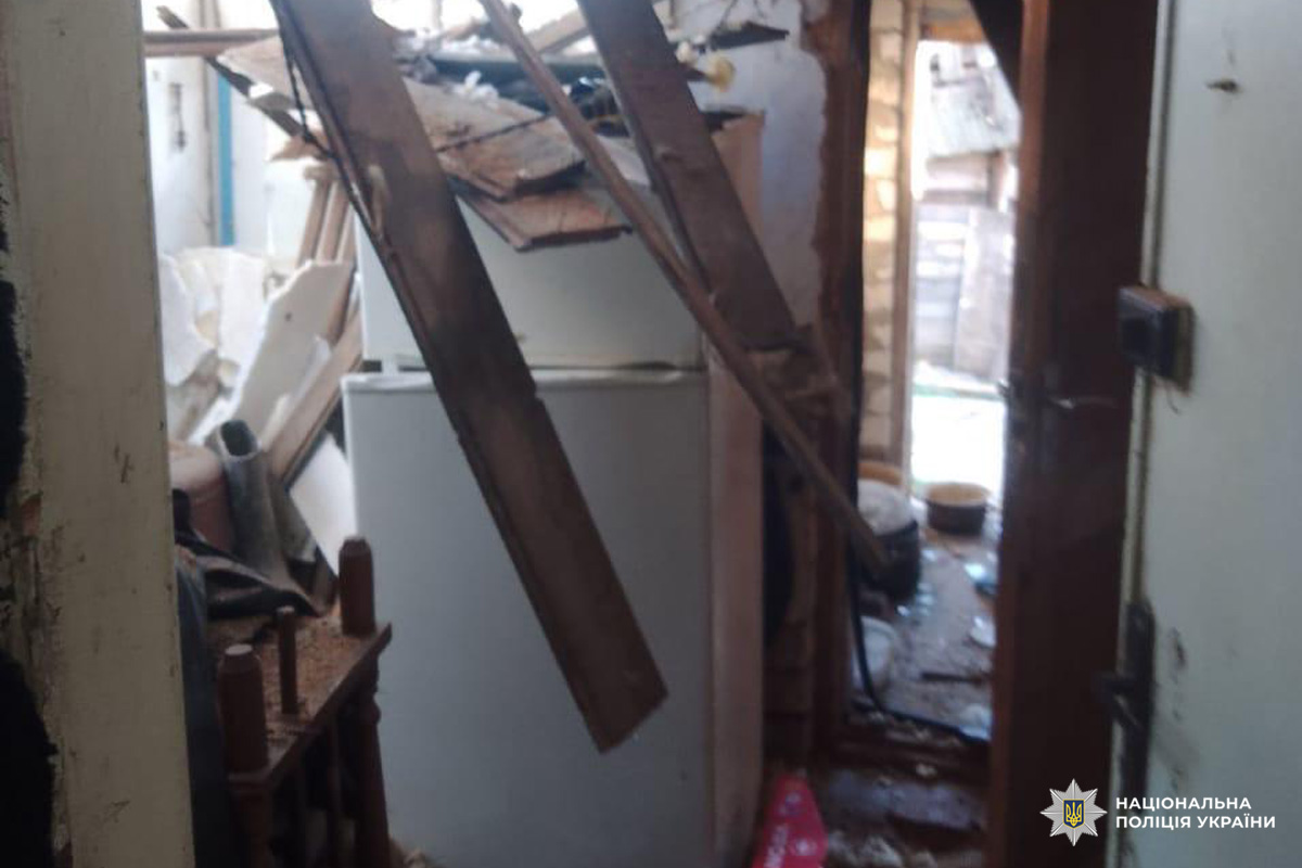 На фото внутрішня частина будівлі з ознаками серйозних руйнувань: обвалені дерев’яні балки, пошкоджені стіни та стеля, побутова техніка серед уламків. Видно холодильник, частково перекритий завалами.