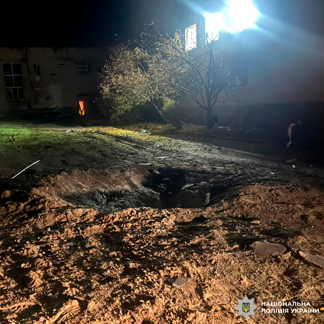 Нічна зйомка місця вибуху: глибока вирва, пошкоджені будівлі, уламки навколо.