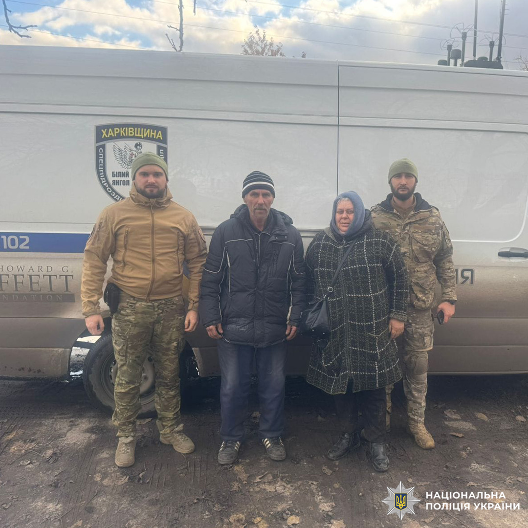 Співробітники Національної поліції України на Харківщині поруч із двома цивільними чоловіком і жінкою в зимовому одязі.