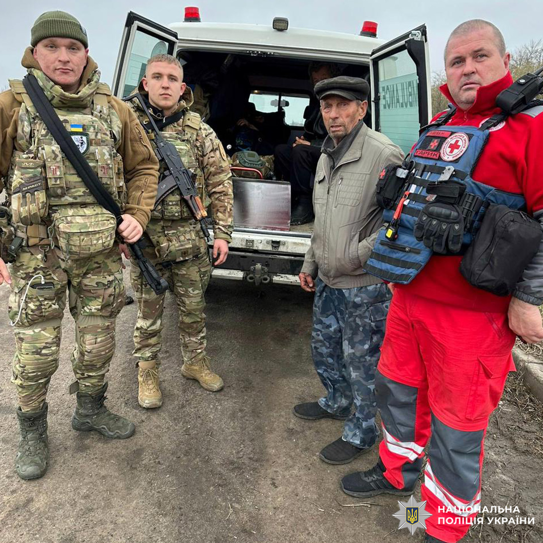 Співробітники Національної поліції України та представник Червоного Хреста біля службового мікроавтобуса з відкритими дверима. Поруч цивільний чоловік у камуфльованих штанах. Поліцейські озброєні.