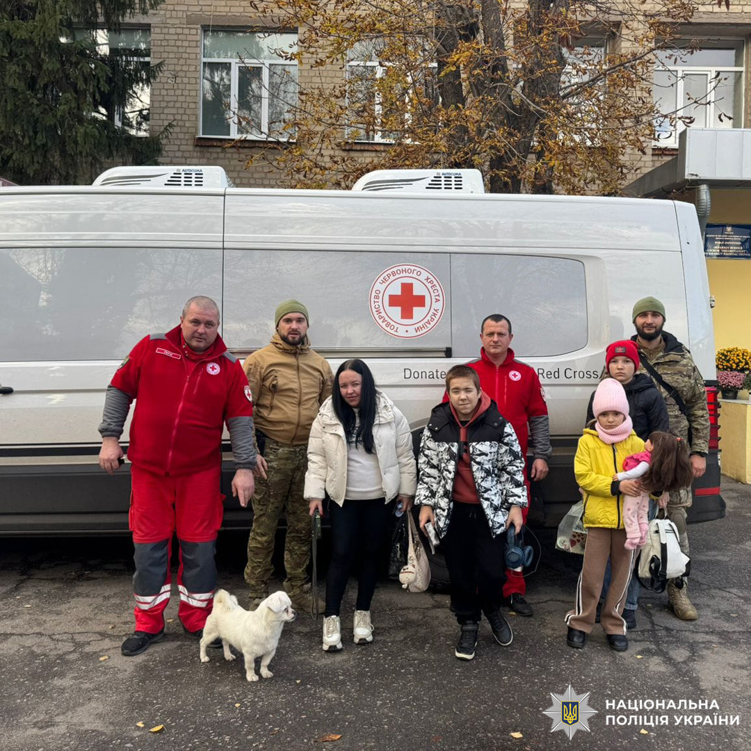Представники Національної поліції України, Червоного Хреста та цивільні особи серед них діти з собакою, біля гуманітарного мікроавтобуса з емблемою Червоного Хреста.