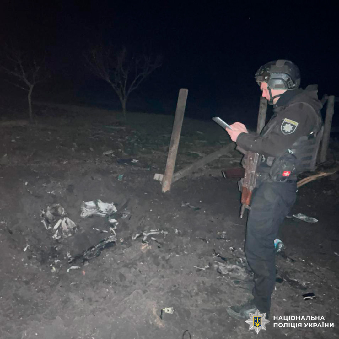 Поліцейський документує вирву від вибуху вночі. На землі уламки, навколо темна місцевість.