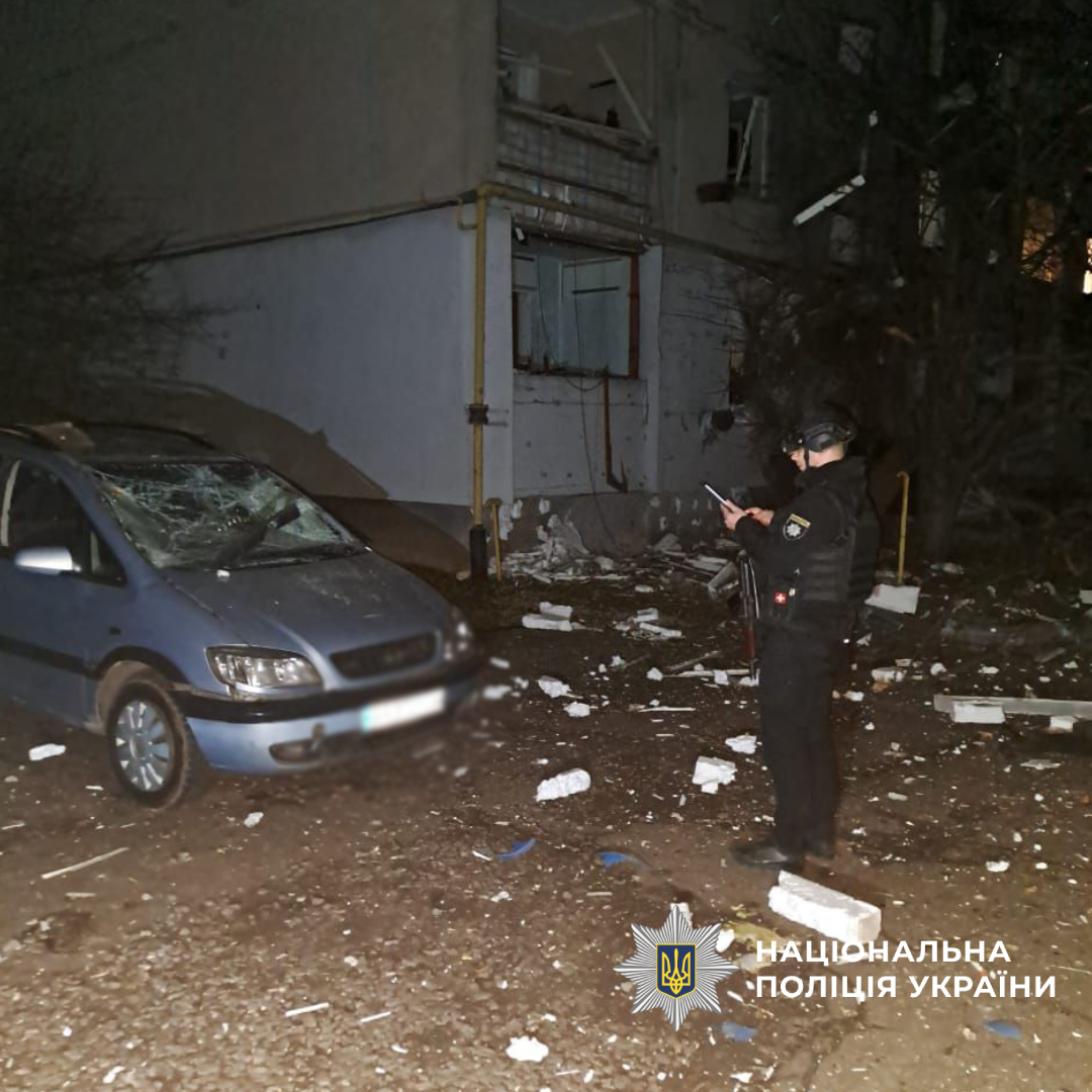 Поліцейський поруч з, розбитою внаслідок обстрілу, автівкою