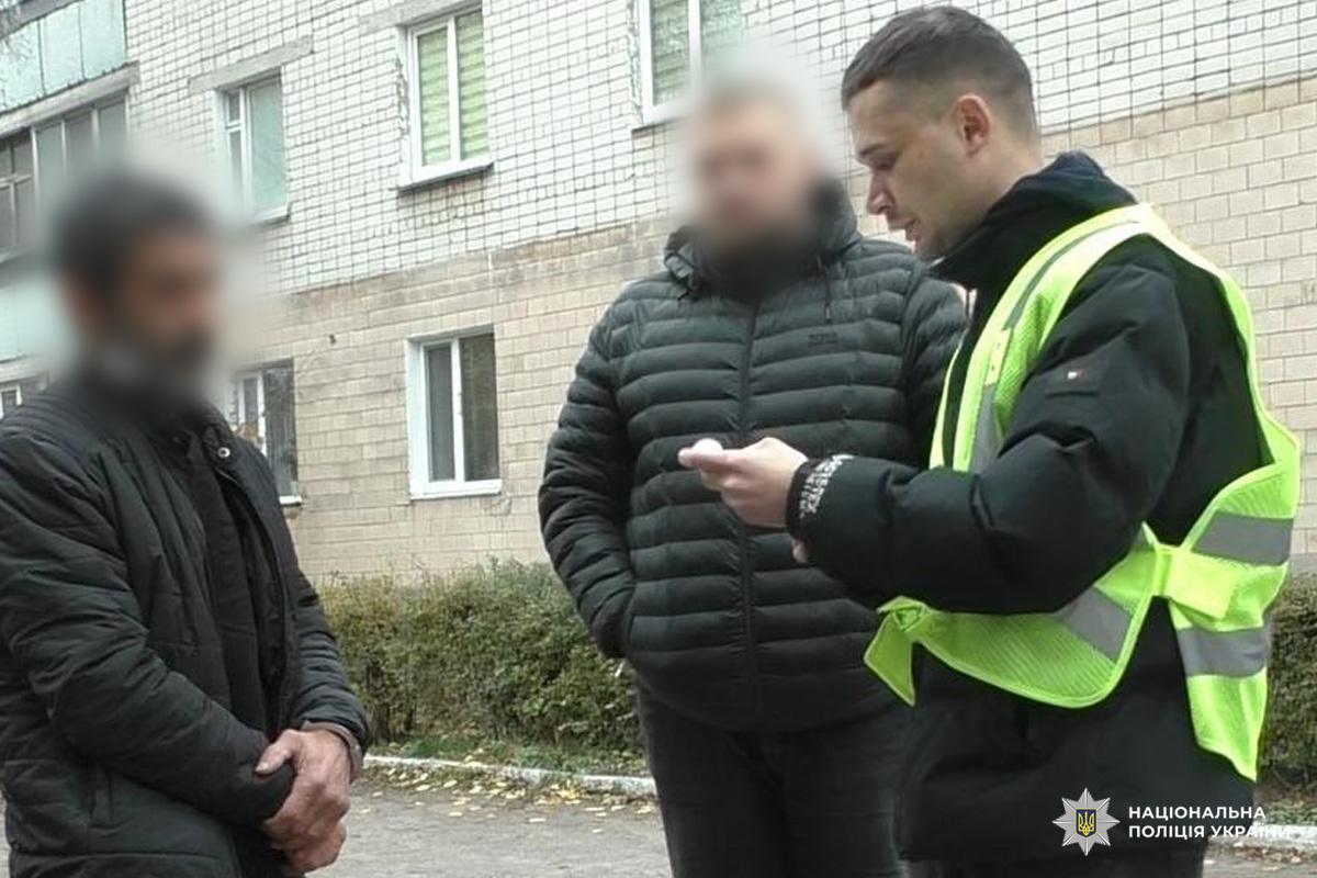 Співробітник поліції у світловідбивальному жилеті спілкується з двома громадянами біля багатоквартирного будинку.