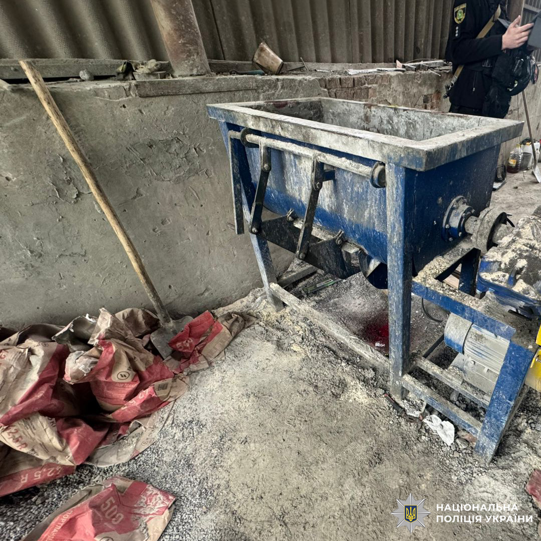 Змішувальна машина для будівельних матеріалів, розірвані мішки з порошкоподібною речовиною та забруднена підлога. Частково видно співробітника поліції, що свідчить про проведення перевірки або слідчих дій.