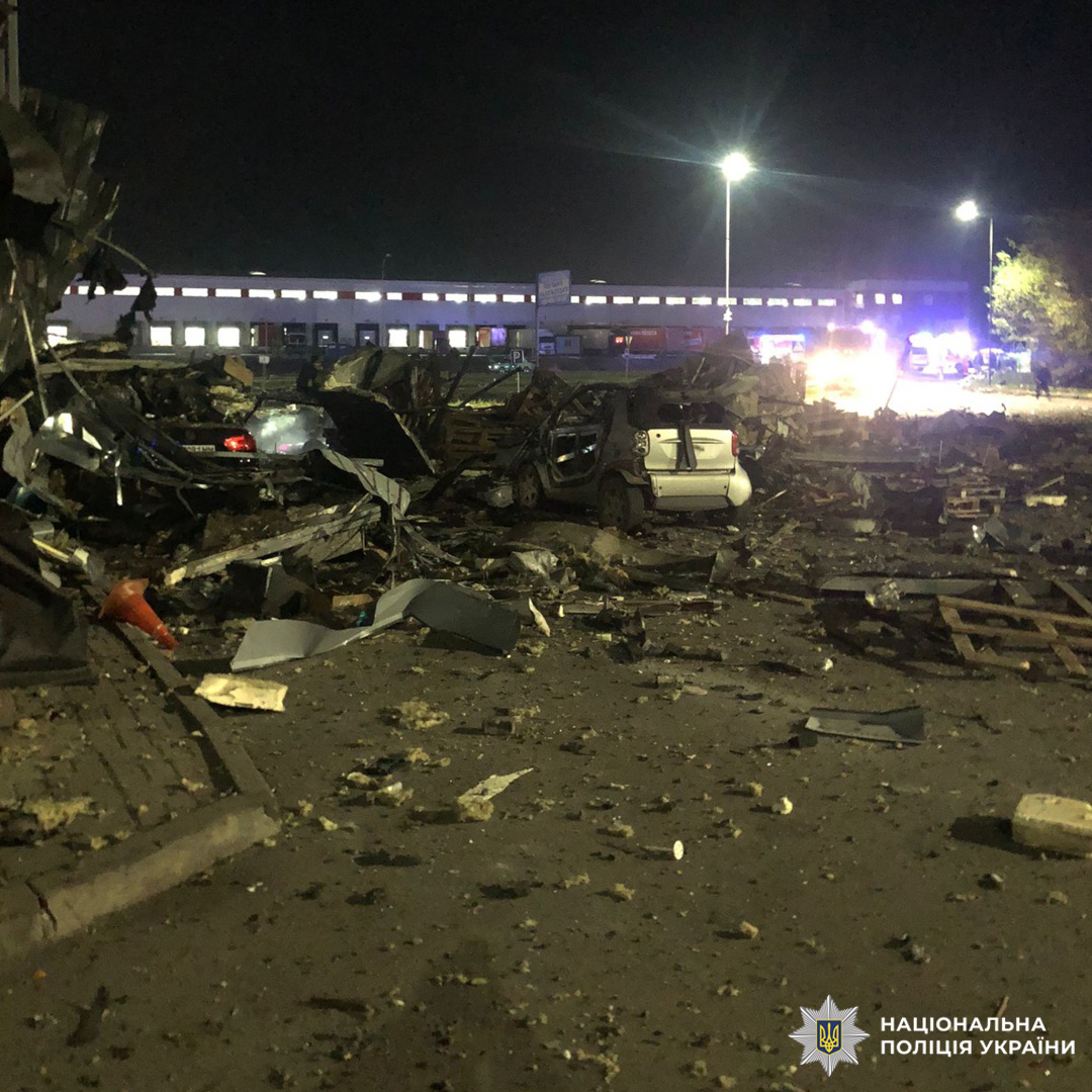 Нічна сцена масштабних руйнувань: серед уламків понівечені автомобілі, зокрема білий легковик у центрі. Територія засипана металевими конструкціями та залишками будівель.