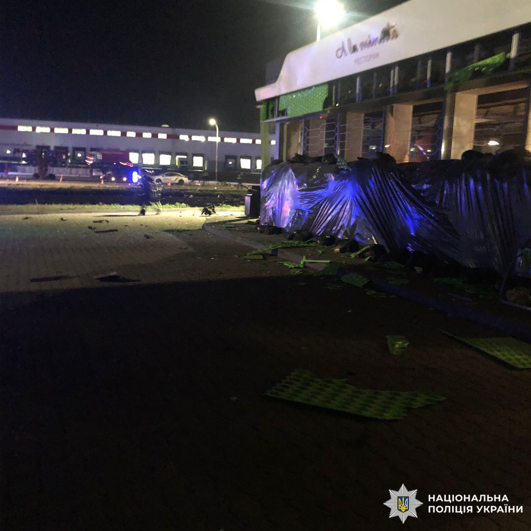 Нічна сцена біля пошкодженого магазину : перед фасадом уламки зелених панелей та інших матеріалів.