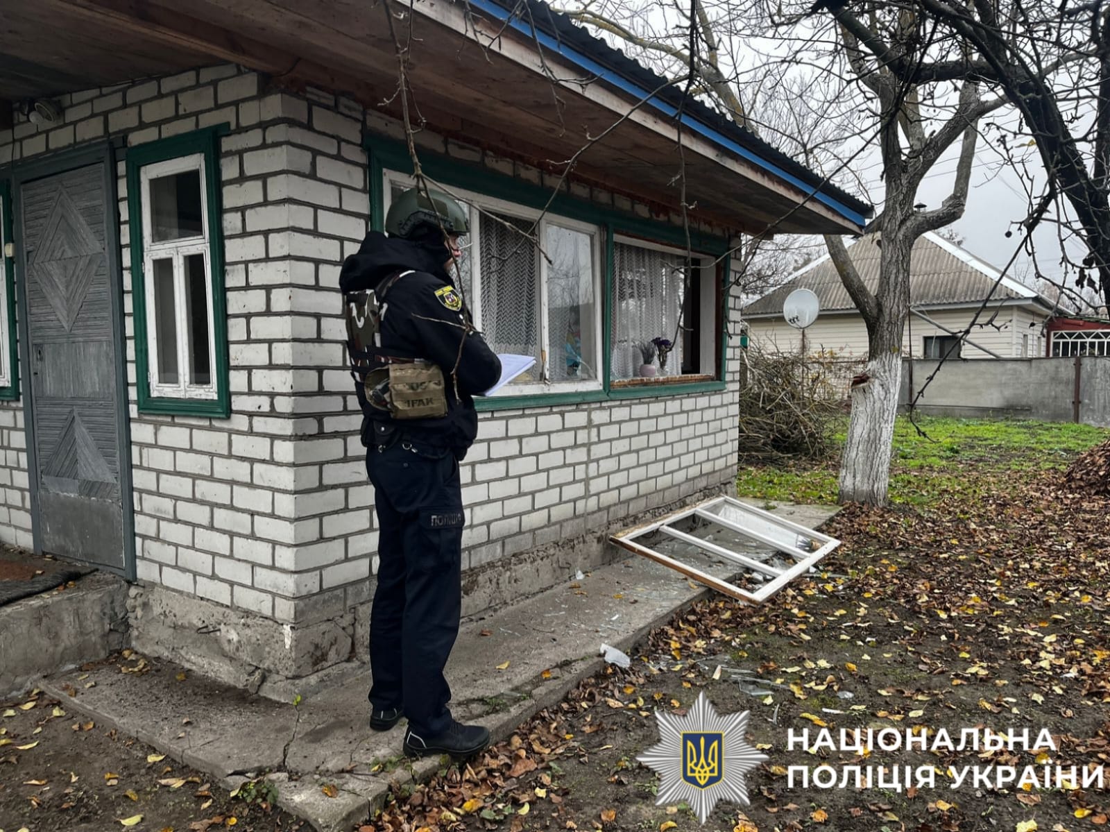 На фото поліцейський на фоні пошкодженого будинку.