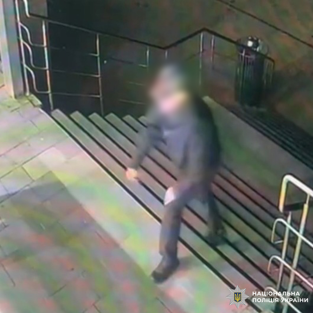 Кадр із камери спостереження: особа в темному одязі підіймається сходами на вулиці вночі. Обличчя розмито з метою захисту персональних даних. На фоні плитка, металеві поручні та темна стіна.