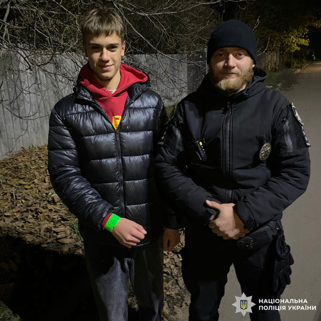 Поліцейський разом із підлітком. На обох теплий одяг, на зап’ястку хлопця — світловідбивний браслет.