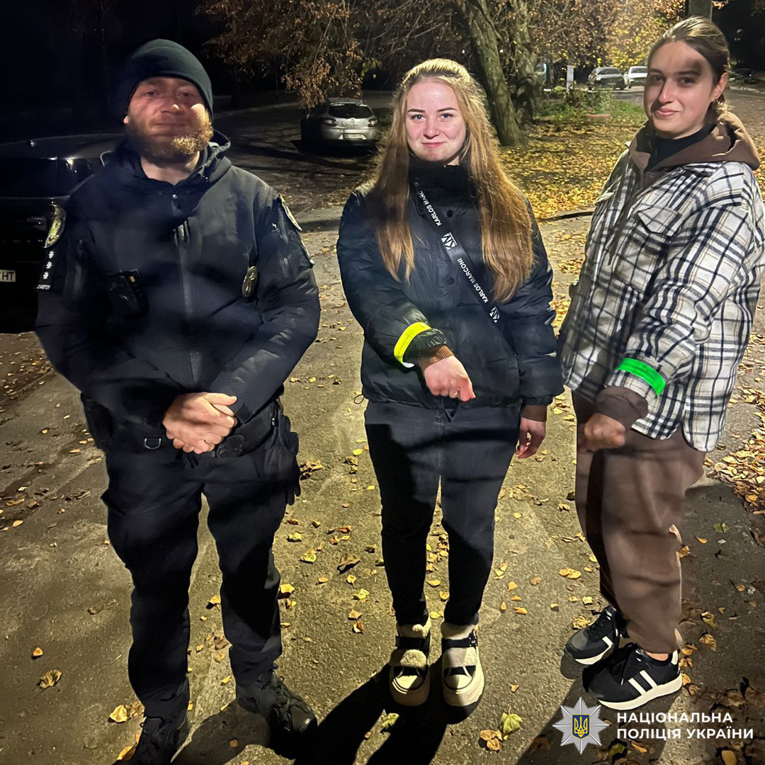Поліцейський разом із двома дівчатами, які носять світловідбивні браслети під час вечірньої прогулянки.