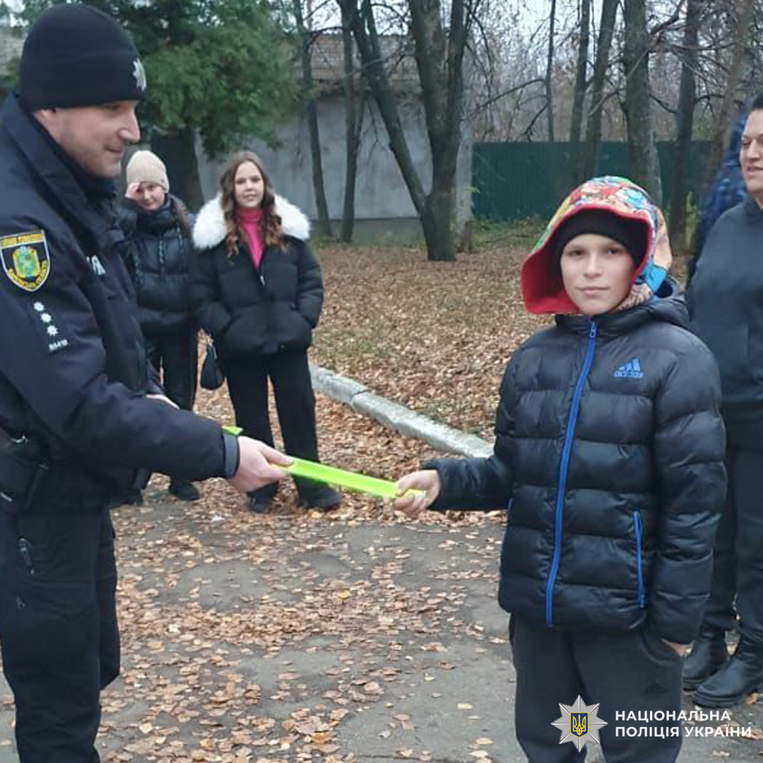 Поліцейський під час профілактичної бесіди вручає хлопчику світловідбивний елемент.