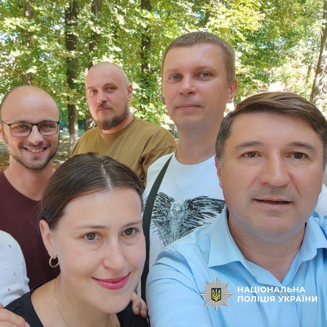 П'ятеро дорослих позують для селфі на тлі зелених дерев у парку. Стоять близько один до одного, усміхаються, дивляться в камеру.