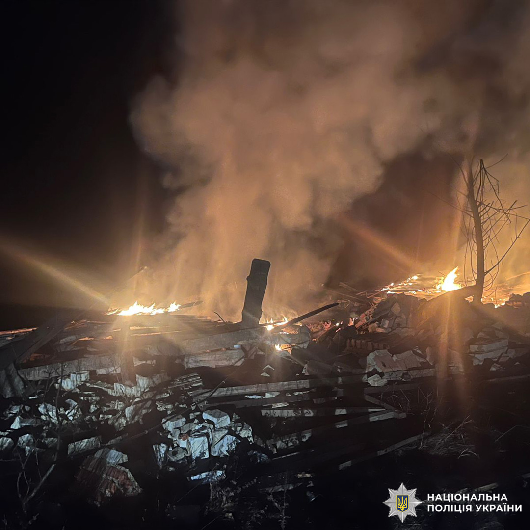 Нічна сцена масштабної руйнації: палаючі уламки зруйнованої конструкції, густий дим, розкидане бетонне та металеве сміття.