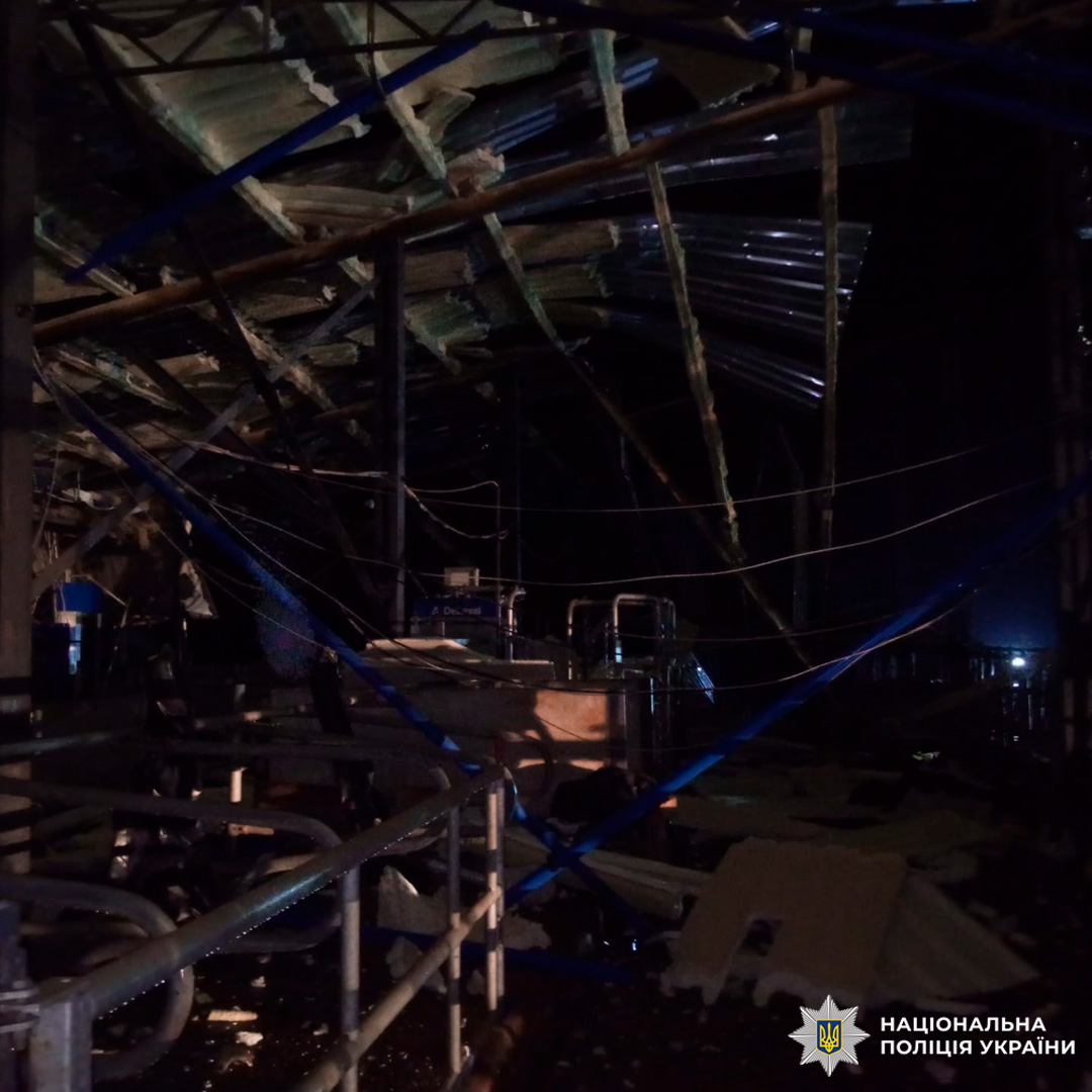 На фото внутрішнє приміщення фермерського або виробничого об’єкта з ознаками серйозних пошкоджень. Частково обвалена покрівля, деформовані металеві конструкції, на підлозі уламки будівельних матеріалів та обладнання.