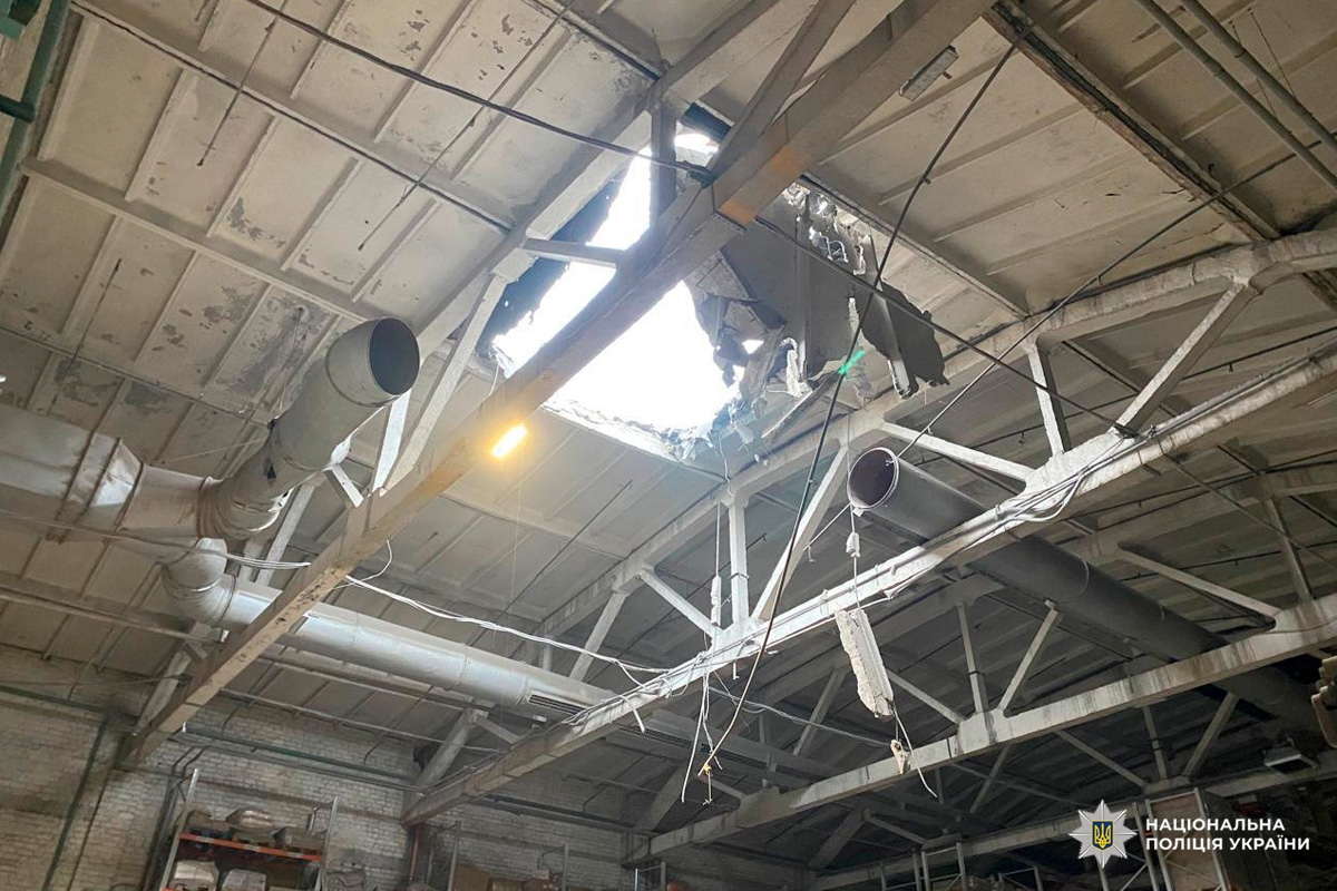 Промислове приміщення з пробитим дахом і пошкодженими конструкціями. Видно труби, балки та уламки.
