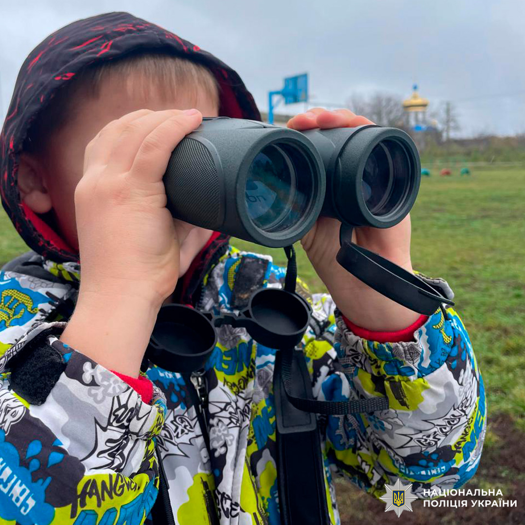 На фото дитина, яка тримає бінокль, одягнена в куртку з графічними елементами.