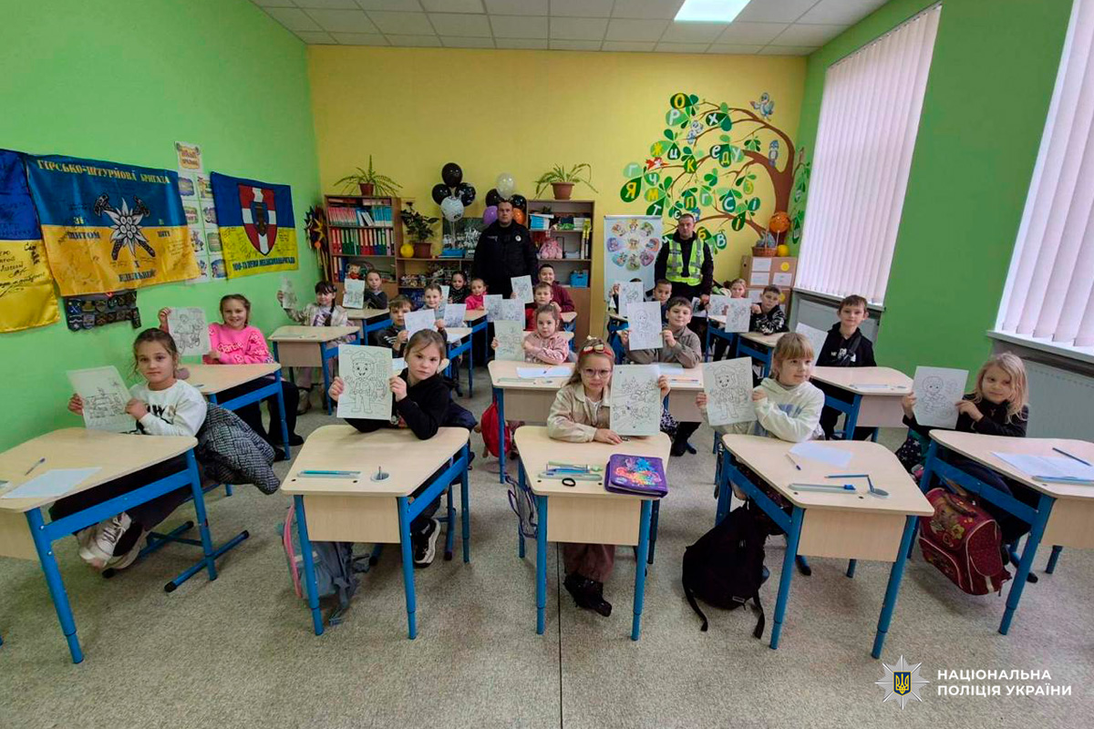 Учні в класі, які демонструють розмальовані аркуші з персонажами. Приміщення оформлене яскравими малюнками, освітніми плакатами та прапорами.