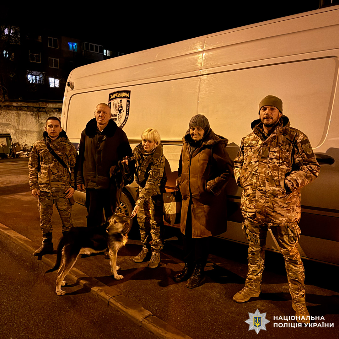 П’ятеро осіб перед службовим автомобілем. Троє у формі, один із них тримає на повідку службового собаку. Двоє у цивільному зимовому одязі.