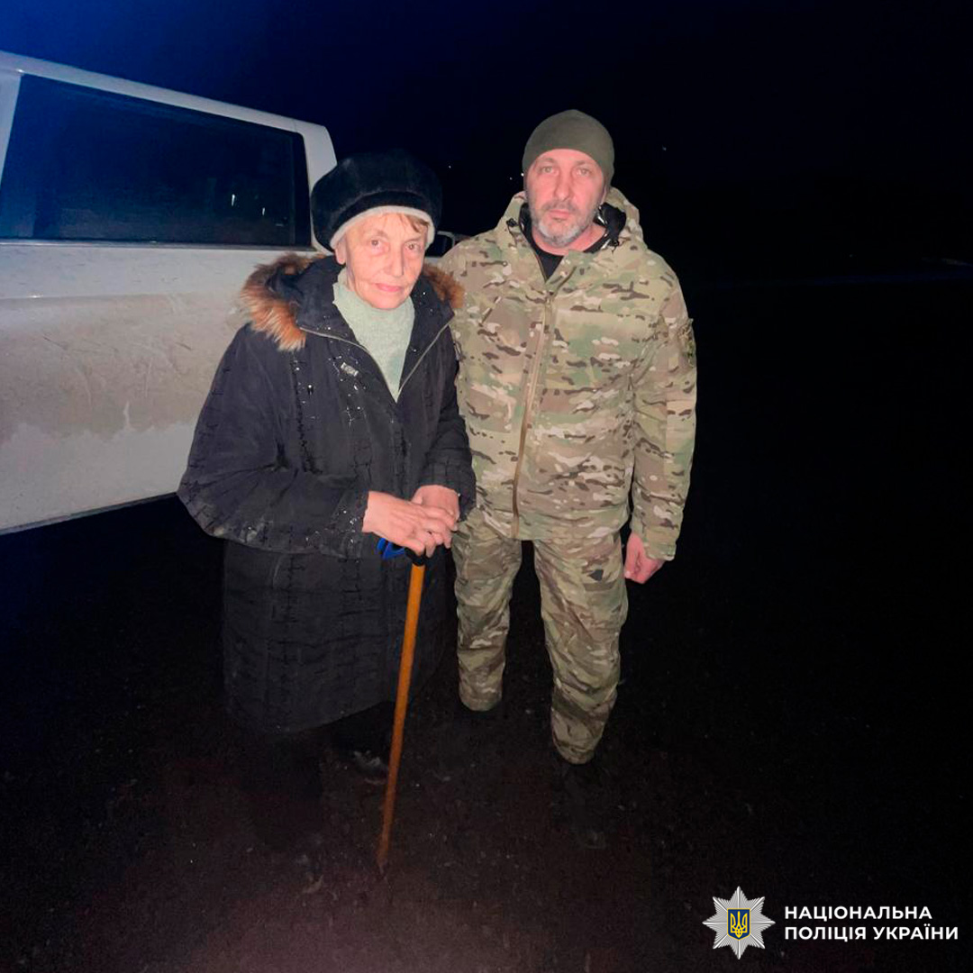 Двоє осіб перед службовим автомобілем. Один у цивільному зимовому одязі з тростиною, другий у камуфляжній формі. Знімок зроблено вночі.