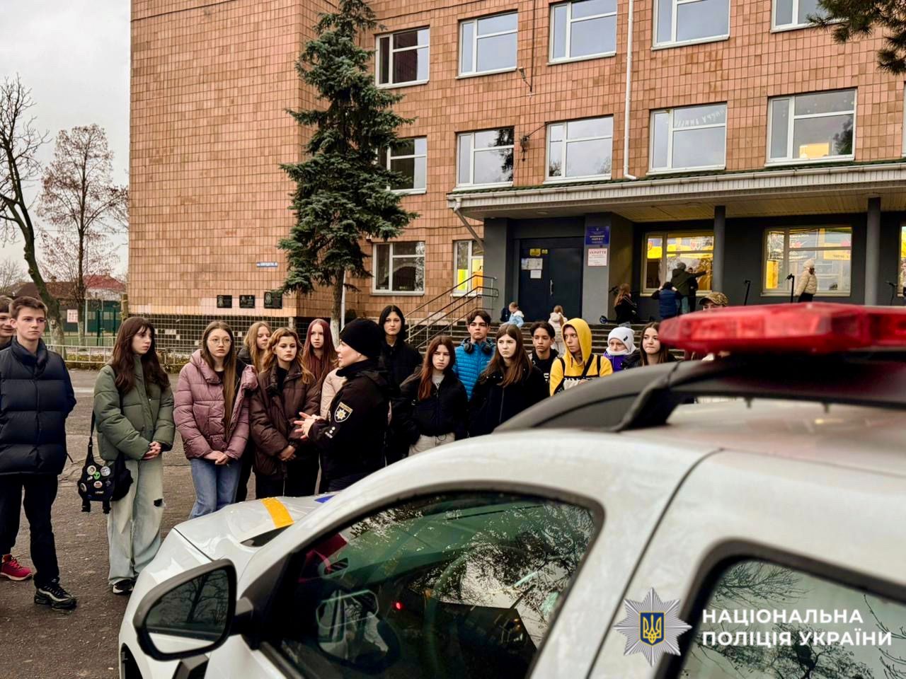 На фотографії зображено дітей та працівника поліції, яка проводить для них пізнавальний захід.