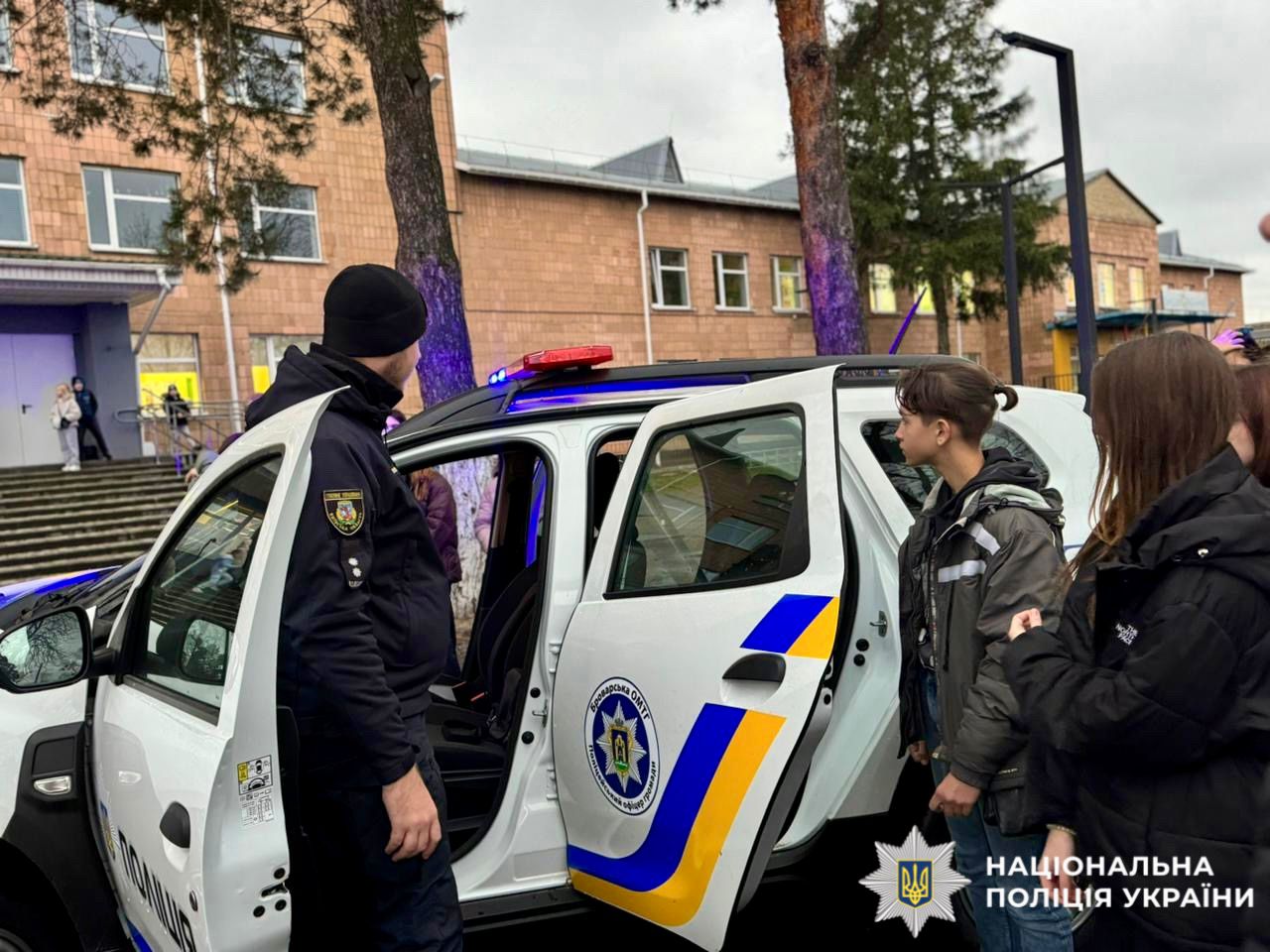 На фотографії зображено дітей та працівника поліції, який проводить для них пізнавальний захід.