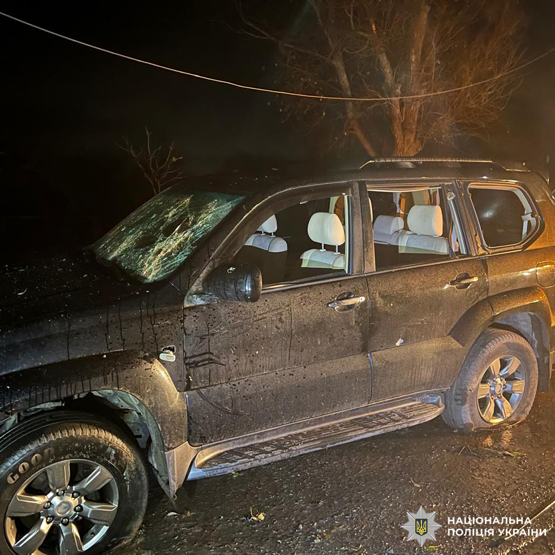 Темний позашляховик із розбитим лобовим і боковими вікнами стоїть на мокрій дорозі вночі.