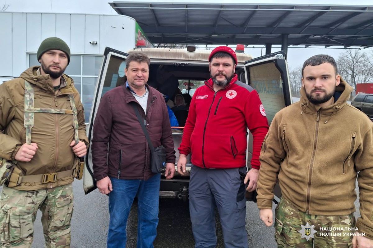 Четверо людей біля відкритого фургона: поліцейські, цивільні та представник гуманітарної організації в червоній куртці з емблемою Червоного Хреста.