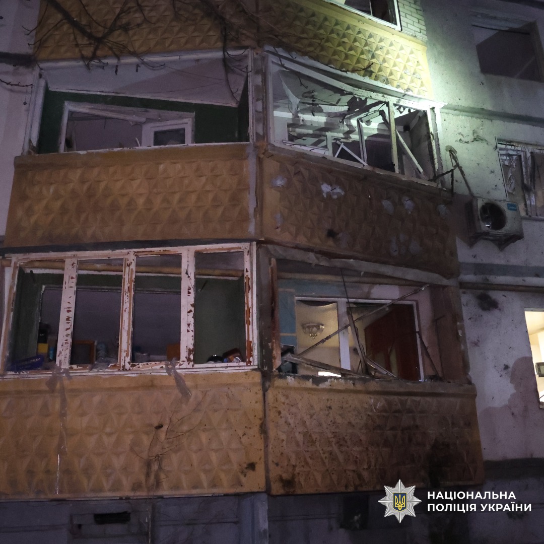 Пошкоджений житловий будинок із зруйнованими балконами та вибитими вікнами. Руйнування зосереджені на нижніх поверхах. Видимі уламки, відкриті квартири.