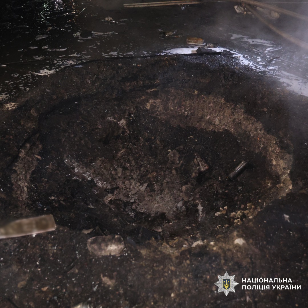 Велика вирва після вибуху. Обгорілий ґрунт, уламки, дим або пара. Нічна зйомка.