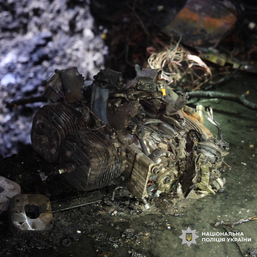 Обгорілий двигун, ймовірно від безпилотніка лежить серед уламків на мокрій поверхні. Метал деформований після вибуху або пожежі.