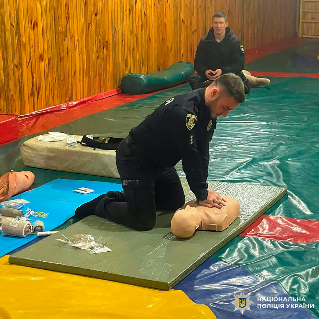 Поліцейський проходить тренування з надання першої допомоги, виконуючи компресії на манекені в навчальному залі.